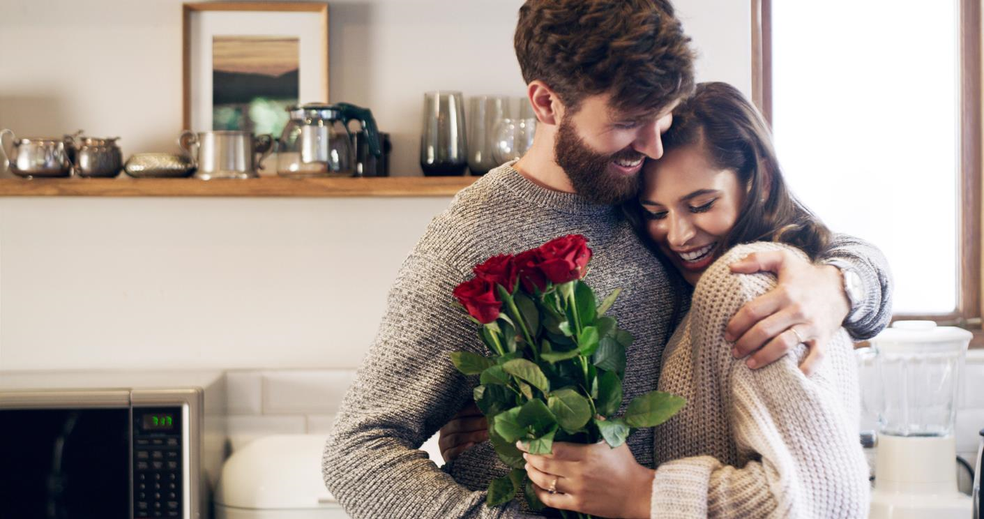 Man and woman smiling and embracing, with red roses in woman's hand. 
