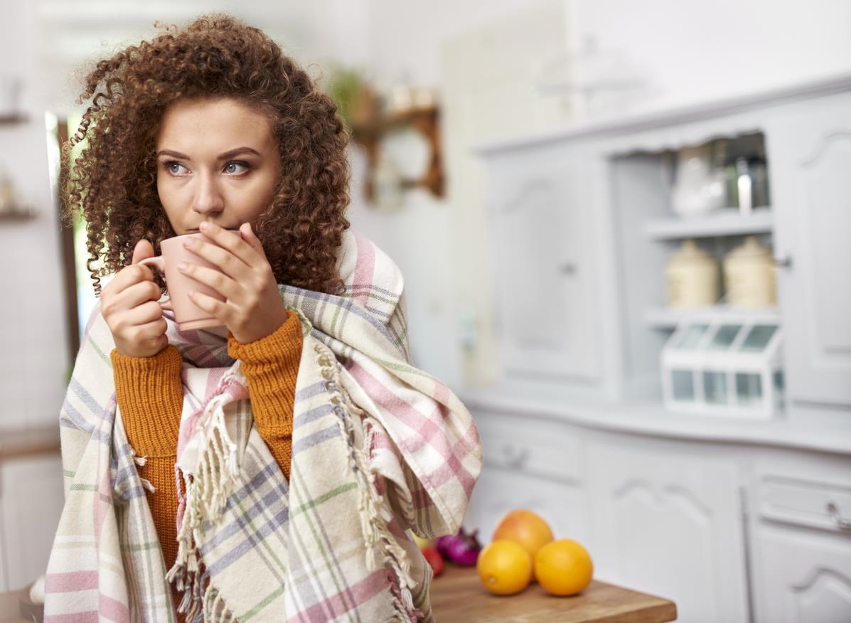 Woman drinking out of mug, wrapped in scarf. 