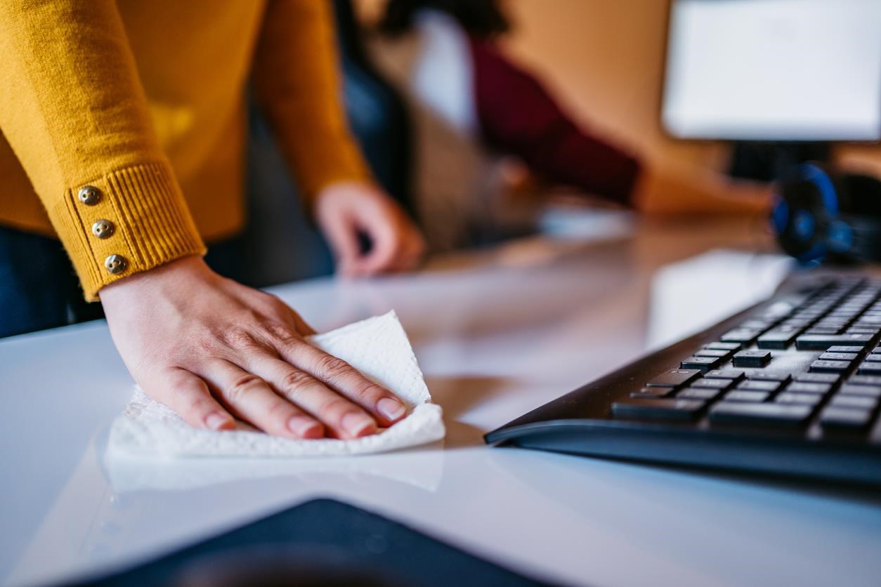 Woman wiping down a desk next to a keyboard.