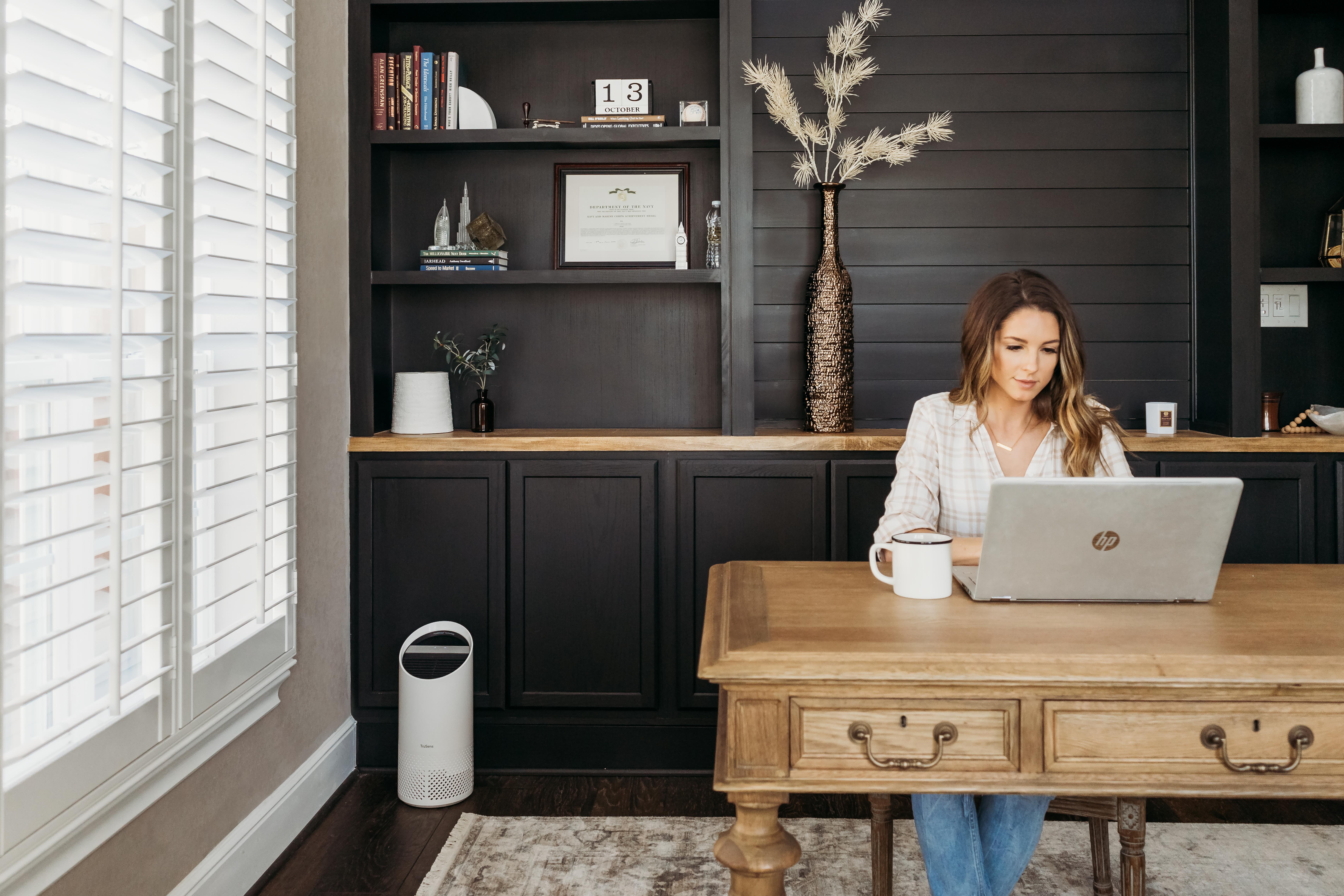 Woman sitting in a home office with a small TruSens Air Purifier in the corner