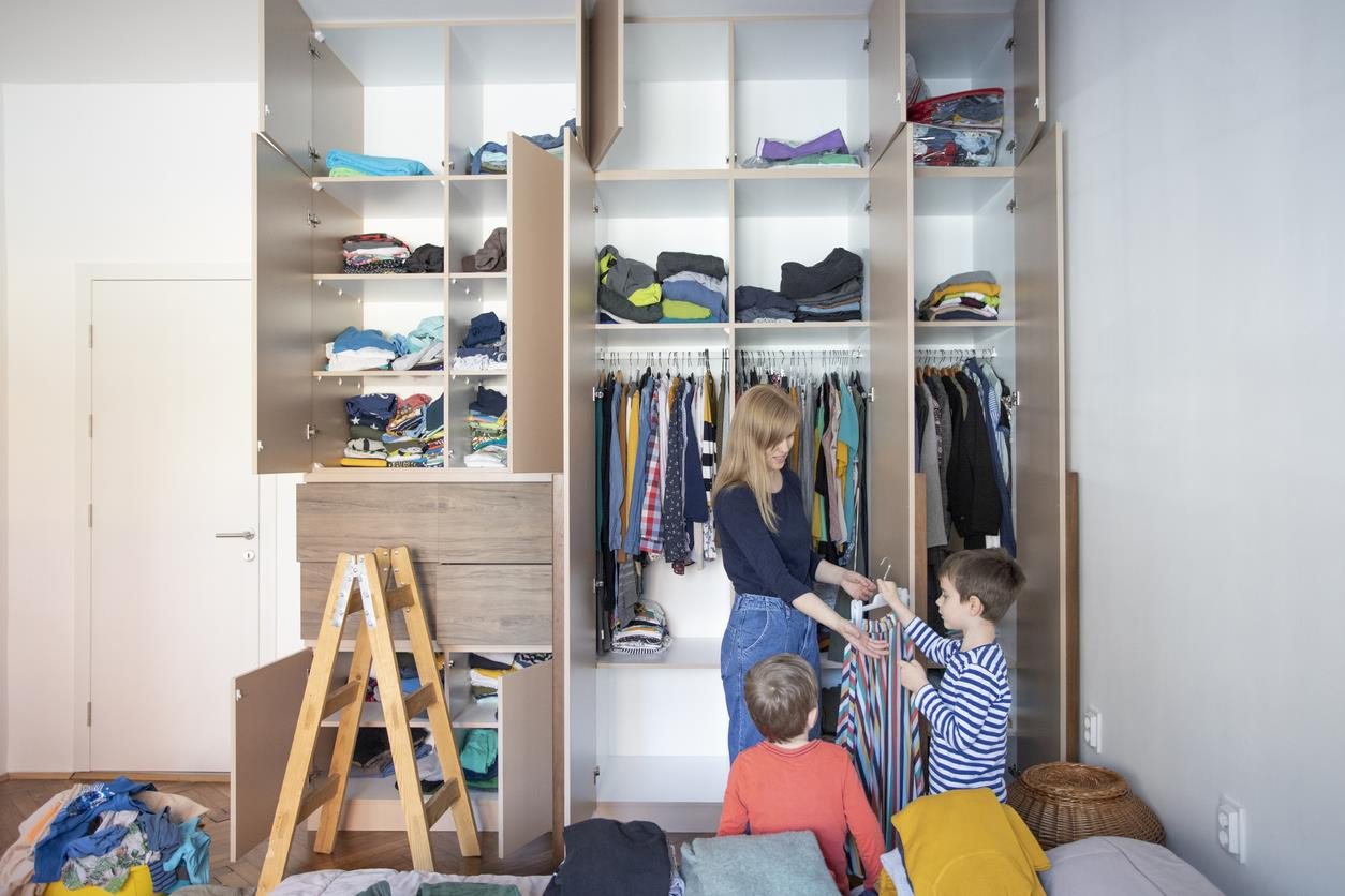 Mom and her two young boys rearranging a close with all the doors opened. 