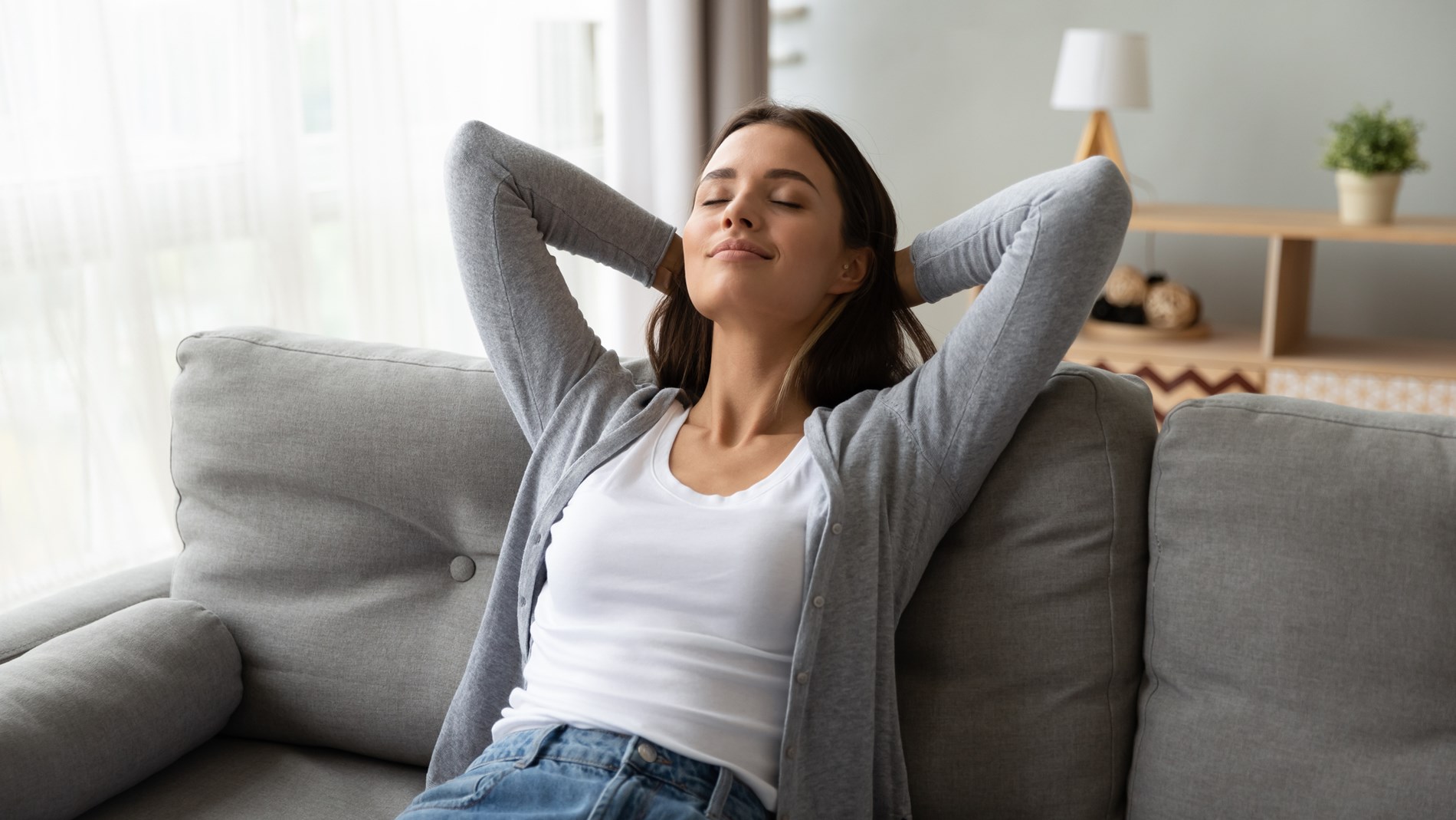 Woman sitting on a couch with her arms behind her head and eyes closed. 