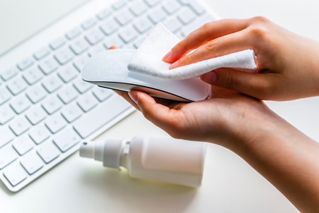 Cleaning a computer mouse with a wipe. 