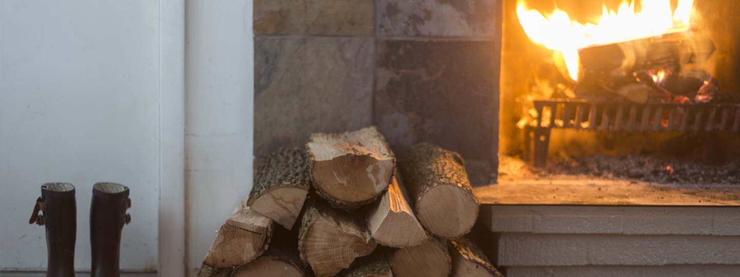 A lit fireplace with a pile of wood next to it. 
