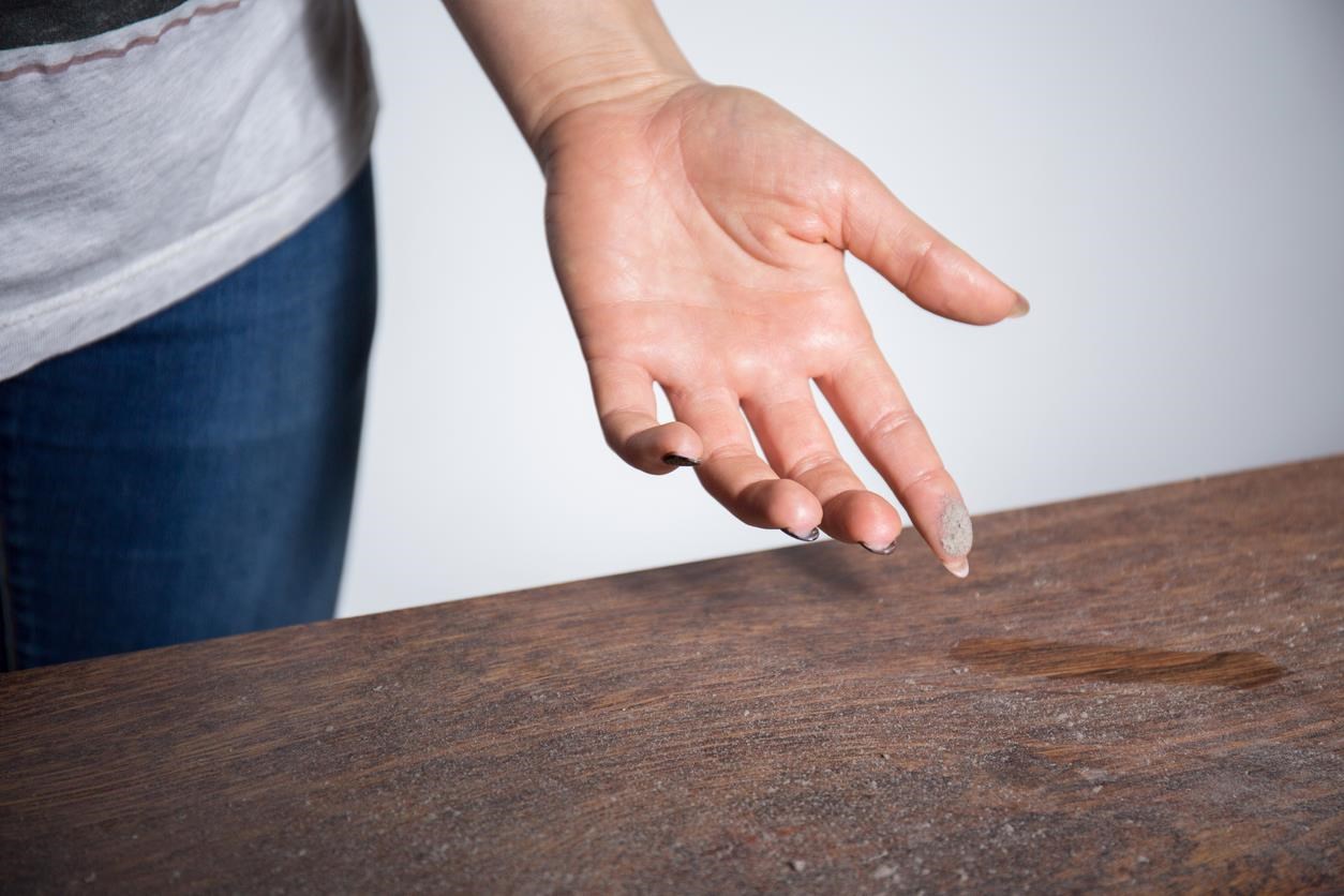 Woman using a finger to swipe a layer of dust off a dusty wood table. 