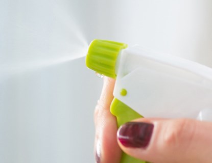 Person's hand pressing handle, spraying liquid out of a cleaning spray bottle. 