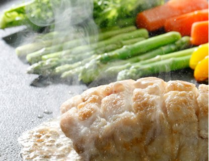 Chicken and vegetables cooking on a non-stick flat top. 