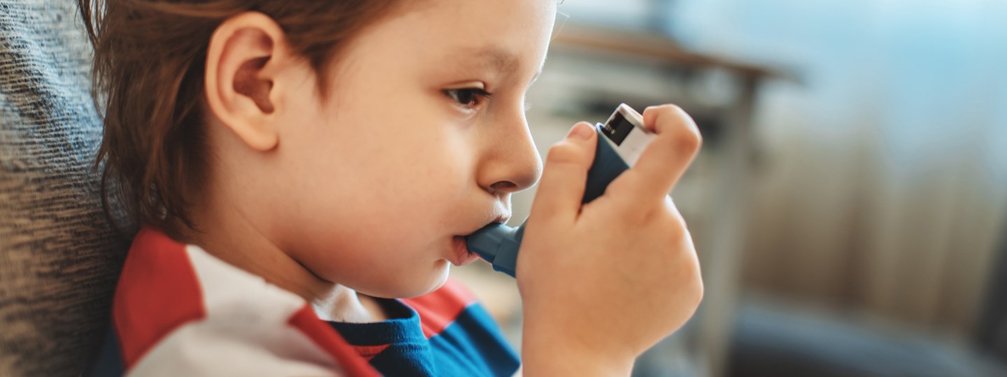 Kid sitting on the couch breathing in their inhaler. 