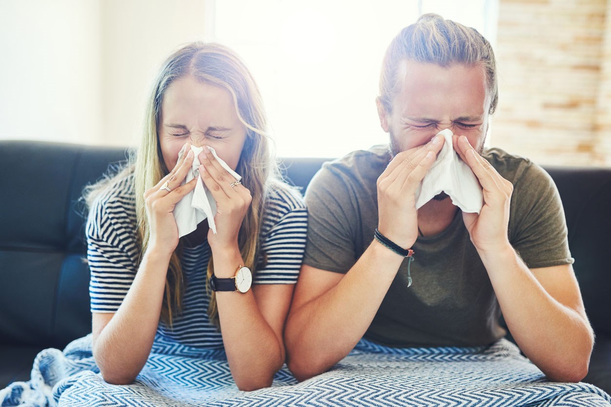 Woman and man both blowing their noses into tissues.