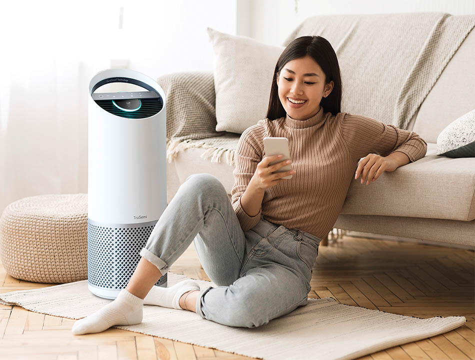 Woman sitting on floor holding smartphone next to air purifier