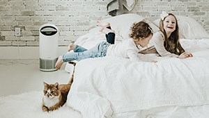 TruSens Air Purifier in the background with kids on a bed with a catwith a woman in the background 