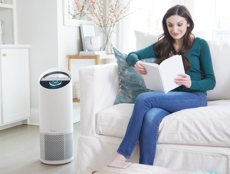Woman reading a book on the couch next to an air purifier